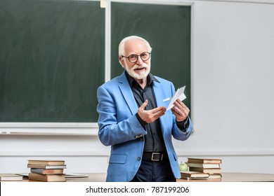 Smiling Grey Hair Professor Holding Paper Plane In Lecture Hall