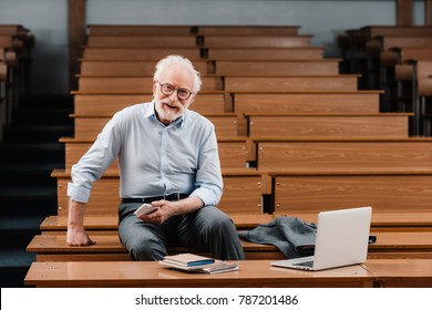 smiling grey hair professor sitting in empty lecture room - Shutterstock ID 787201486