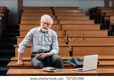 smiling grey hair professor sitting in empty lecture room