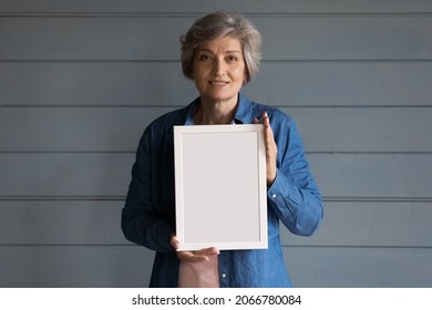 Smiling Grey Haired Senior Lady Head Shot. Positive 60s Mature Adult Woman Holding Blank Empty White Picture Frame, Standing At Studio Background, Looking At Camera. Female Portrait