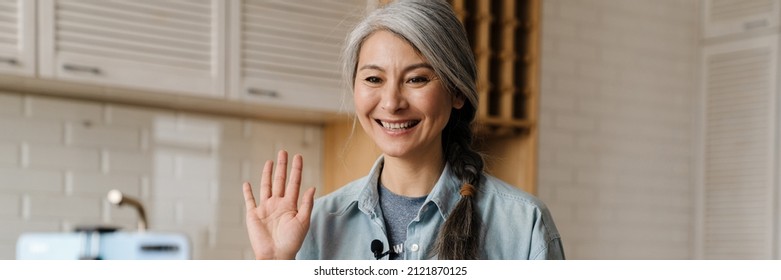 Smiling Grey Woman Gesturing While Taking Selfie Footage On Cellphone At Home