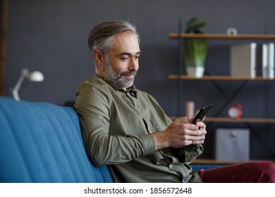 Smiling grey-haired man using mobile phone apps, texting message, browsing internet, shopping online. Looking at smartphone and smiling, sitting at home. Mature people with mobile devices. - Powered by Shutterstock