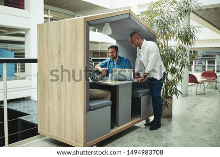 Smiling group of diverse businessmen working together on a project in a meeting pod in the lobby of a modern office