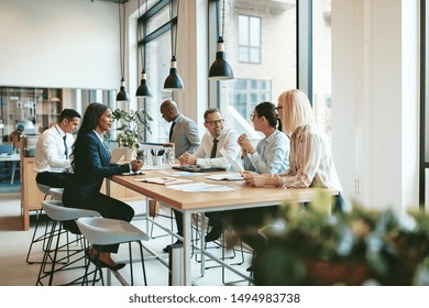 Smiling group of diverse businesspeople discussing paperwork together while having a meeting around a table in a modern office