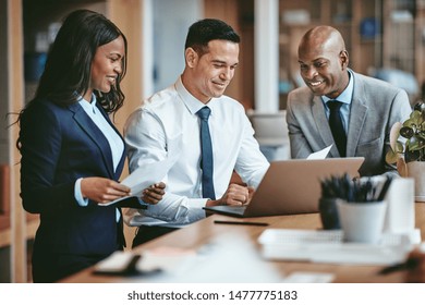 Smiling group of diverse businesspeople going over paperwork together and working on a laptop at a table in an office