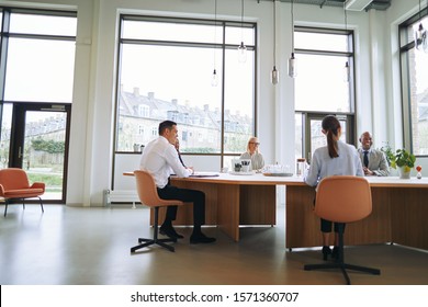 Lächelnde Gruppe von Geschäftsleuten, die während einer Sitzung um einen Sitzungstisch in einem Büro sitzen