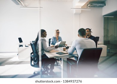 Smiling Group Of Diverse Coworkers Talking Together During A Meeting Around A Table Inside Of A Glass Walled Office