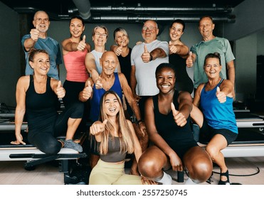 Smiling group of diverse men and women in sportswear giving the thumbs up together after an exercise class in a pilates gym - Powered by Shutterstock