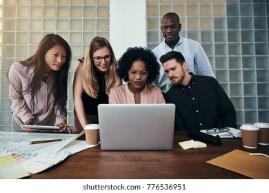 Smiling Group Of Diverse Work Colleagues Talking And Working Together On A Laptop At A Table In A Modern Office