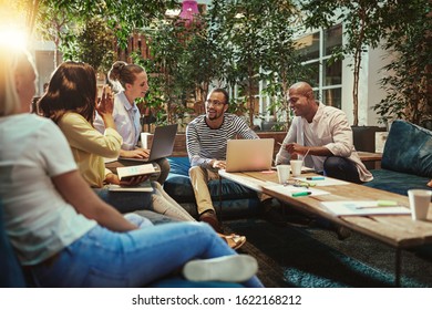Smiling group of diverse young businesspeople working together on sofas around a coffee table in an office lounge