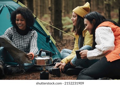 Smiling Group Of Diverse Young Female Friends Sitting At Their Forest Campsite Making Coffee And Reading A Trail Map