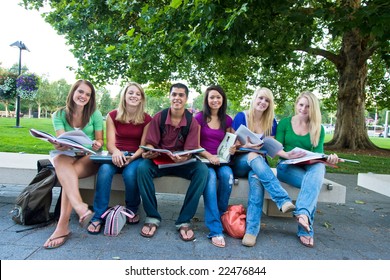 Smiling Group Of Five High School Girls And One Boy Sitting On A Bench Holding Books. Horizontally Framed Photo.
