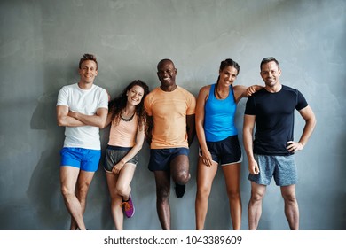 Smiling group of friends in sportswear laughing while standing arm in arm together in a gym after a workout