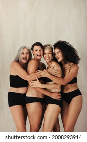 Smiling Group Of Natural Women Embracing Their Bodies Together. Four Body Positive Women Of All Ages Embracing Each Other While Wearing Black Underwear Against A Studio Background.