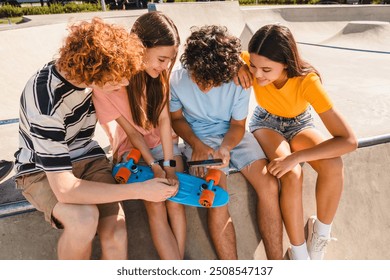 Smiling group of teenagers classmates students school pupils friends boys girls in casual watching funny video laughing out having fun using gadgets internet sitting on ramp in skate park - Powered by Shutterstock