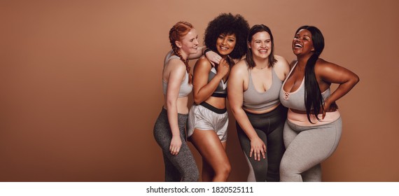 Smiling group of women in different size standing together in sportswear against brown background. Diverse group women looking at camera and laughing. - Powered by Shutterstock