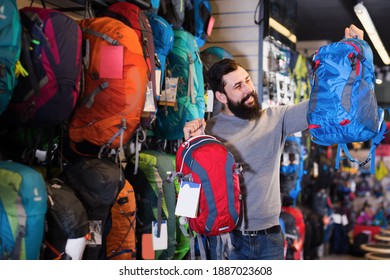 Smiling Guy Customer Examining Backpacks In Sports Equipment Store