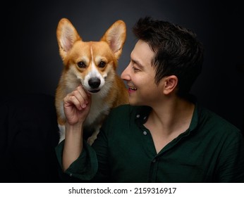 Smiling Guy With Cute Corgi Dog At Black Background In Studio