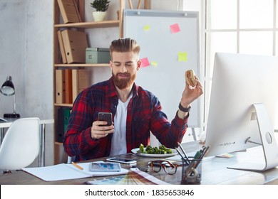 Smiling Guy Eating Burger At Workplace While Using Phone