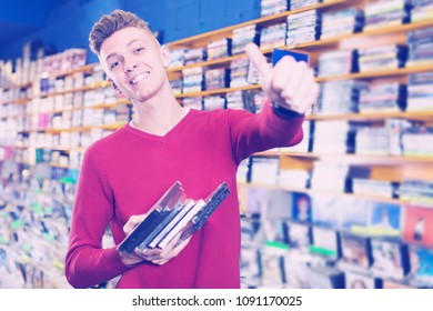 Smiling guy holding stack of DVDs bought in store giving thumbs up
