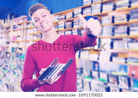 Smiling guy holding stack of DVDs bought in store giving thumbs up
