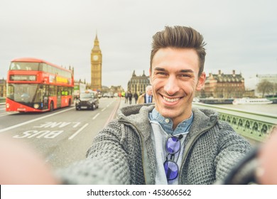 Smiling Guy Take Selfie Photo During Travel In London, England. Traveler Man In Front Of Big Ben Tower Taking Memory Pic With Iconic England Red Bus. Happy People Concept Wandering Around The World.