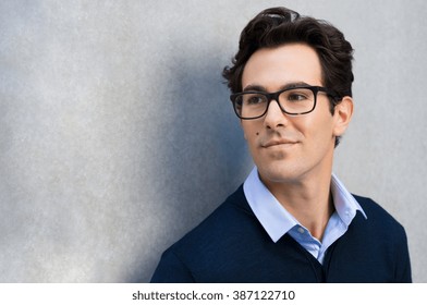 Smiling guy wearing glasses looking away and leaning on grey wall. Portrait of young businessman with eyeglasses thinking about his carrer with copy space. - Powered by Shutterstock