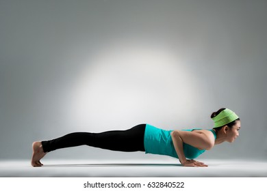 Smiling Gymnastic Female Player Lying On Ground Floor Hands Up Body Performing Pushup Posture At Yoga Fitness Center Studio With Gray Wall Background.