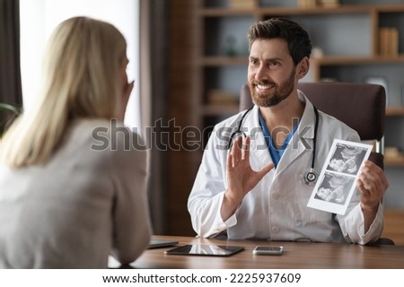 Smiling Gynecologist Doctor Showing Baby Sonography Image To Pregnant Female Patient During Meeting In Office, Happy Reproductive Endocrinologist Sharing News About Successful IVF Treatment