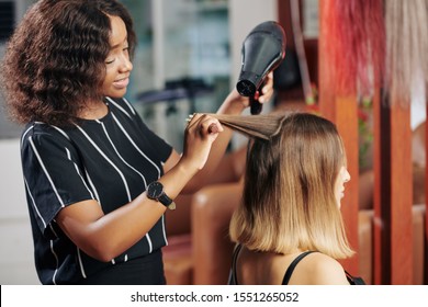 Smiling hairdresser enjoying blowdrying hair of young female client