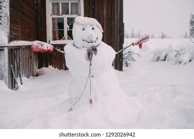 Smiling Handmade Snowman Near The Wooden House In Snowy Winter Weather, No People Around