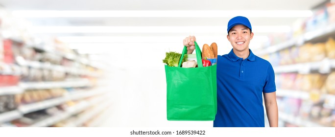 Smiling handsome Asian man holding grocery shopping bag in supermarket banner background with copy spce for food delivery service concept