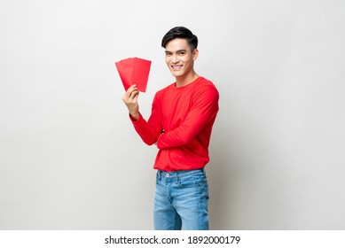 Smiling handsome Asian man holding red envelopes or Ang Pao in studio isolated gray background for Chinese new year concepts