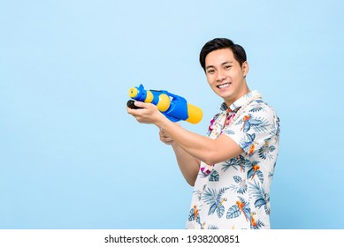 Smiling handsome Asian man playing with water gun isolated on studio blue background for Songkran festival in Thailand and southeast Asia