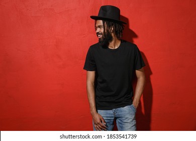 Smiling handsome attractive young african american man guy with dreadlocks 20s wearing black casual t-shirt hat posing looking aside isolated on bright red color wall background studio portrait - Powered by Shutterstock