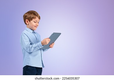 Smiling handsome boy in casual wear standing holding tablet device near empty blue purple wall in background. Concept of inspired kid, social media, mobile application, education, playing game - Shutterstock ID 2256035307