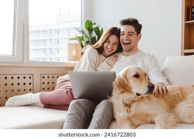 Smiling handsome boyfriend and girlfriend sitting on sofa, hugging, with dog, golden retriever, watching video laughing sitting on comfortable sofa in cozy room. Concept of relationship, dating - Powered by Shutterstock