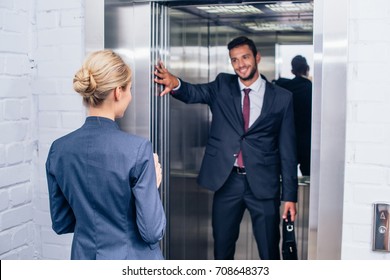 Smiling Handsome Businessman Holding Elevator Door For Woman