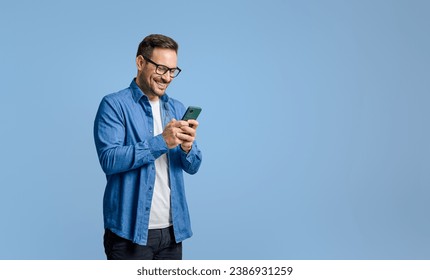 Smiling handsome businessman text messaging over mobile phone while standing on blue background - Powered by Shutterstock