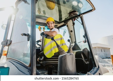 Smiling handsome caucasian worker in overall and with helmet on head driving excavator. - Powered by Shutterstock