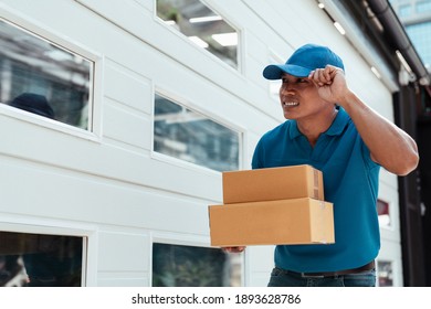Smiling handsome delivery man wearing hat giving parcel cardboard boxes looking for custumer infront of the door.