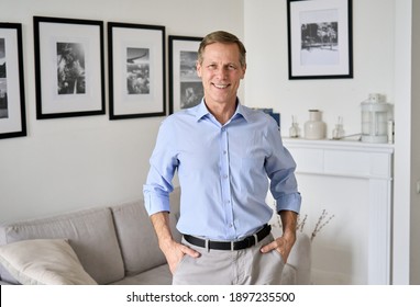 Smiling Handsome Elegant Satisfied 60s Senior Man Standing At Home Interior Looking At Camera. Happy Confident European Wealthy Older Middle Aged Male Retiree Posing In Modern Apartment, Portrait.