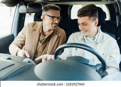 smiling handsome father teaching teen son driving car