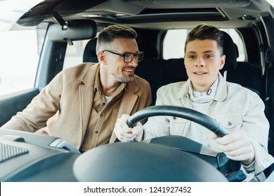 Smiling Handsome Father Teaching Teen Son Driving Car And Looking At Him