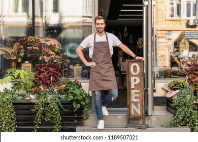 smiling handsome flower shop owner standing on stairs and leaning on open sign - Powered by Shutterstock