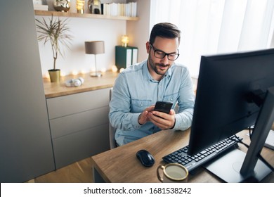 Smiling handsome freelancer working remotely from home. He is using phone. - Powered by Shutterstock