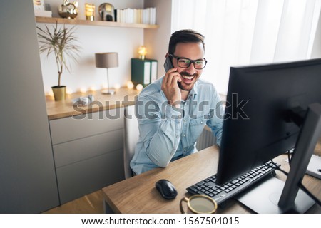 Smiling handsome freelancer working remotely from home. He is speaking on the phone.