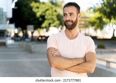 Smiling handsome hispanic man with arms crossed looking away outdoors, copy space. Portrait of bearded hipster wearing casual clothing standing on the street  - Powered by Shutterstock