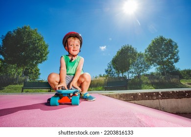 Smiling Handsome Little Boy Sit On The Skate Playing At Skatepark Wearing Helmet On Sunny Summer Day