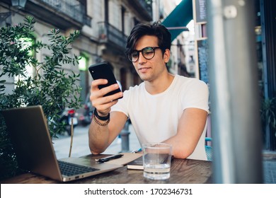 Smiling Handsome Male Influencer Share Content In Social Networks Via Smartphone 4G Internet Connection,smiling Hipster Guy Freelancer Working On Cafe Terrace Using Laptop Computer And Mobile Phone